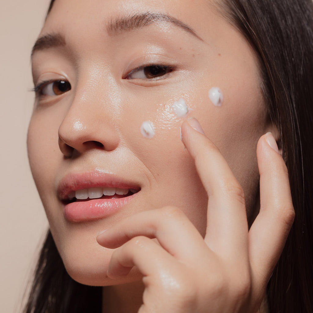 An Asian woman applying cream on her cheek