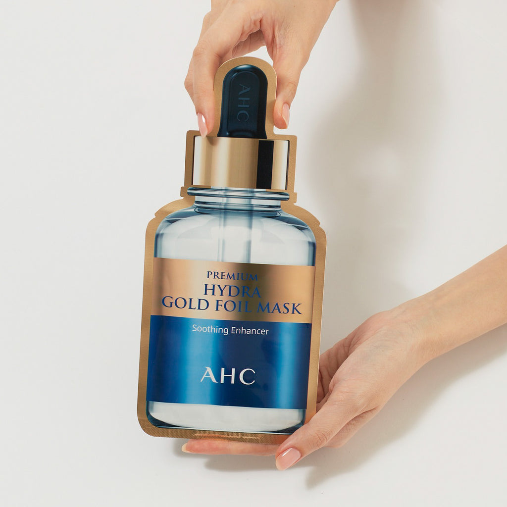 Two hands holding a pack of AHC Premium Hydra Gold Foil Mask