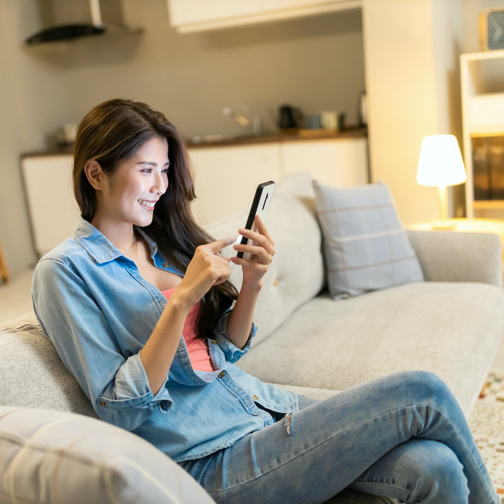 Asian woman use smart phone with blue lights happily at home