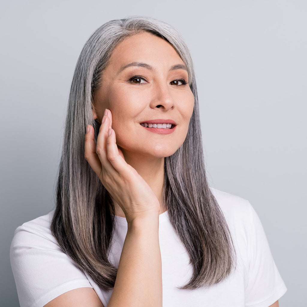 A middle-aged Asian woman with grey hair touching her cheek with her hand